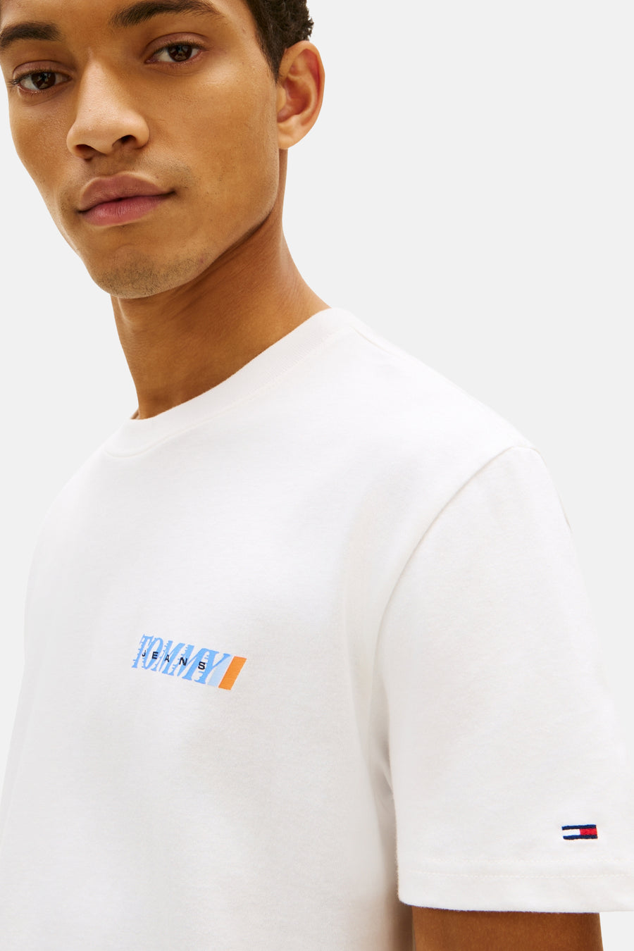 T-shirt blanc de TOMMY JEANS avec logo bleu et orange sur la poitrine et petit drapeau sur la manche.