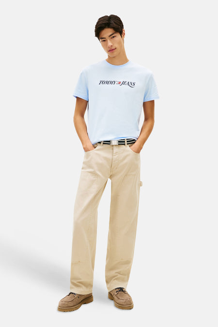 T-shirt bleu clair à manches courtes de TOMMY JEANS, avec logo sur le devant, porté avec pantalon beige et chaussures marron.