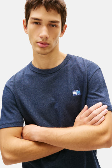 Blauw T-shirt met korte mouwen van Tommy Jeans, gedragen door een man met gekruiste armen.