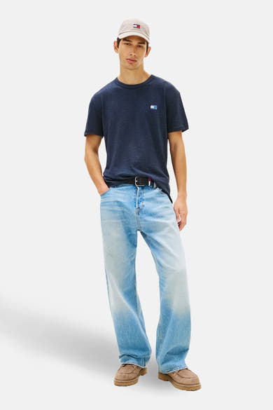 Marineblaues T-Shirt mit kurzen Ärmeln von TOMMY JEANS, mit Logo auf der Brust, getragen mit einer weiten Jeans und einer Kappe.
