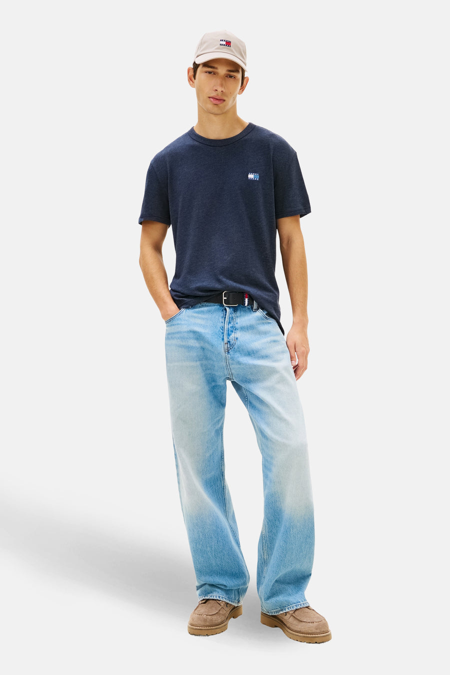 Marineblaues T-Shirt mit kurzen Ärmeln von TOMMY JEANS, mit Logo auf der Brust, getragen mit einer weiten Jeans und einer Kappe.