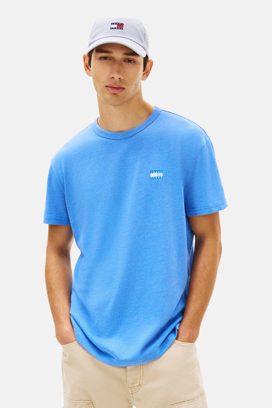 T-shirt bleu à manches courtes de TOMMY JEANS, porté avec un pantalon beige et une casquette.