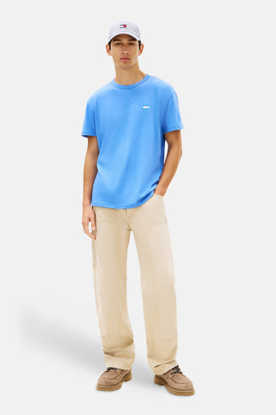 T-shirt bleu à manches courtes de TOMMY JEANS, porté avec un pantalon beige et des chaussures marron.
