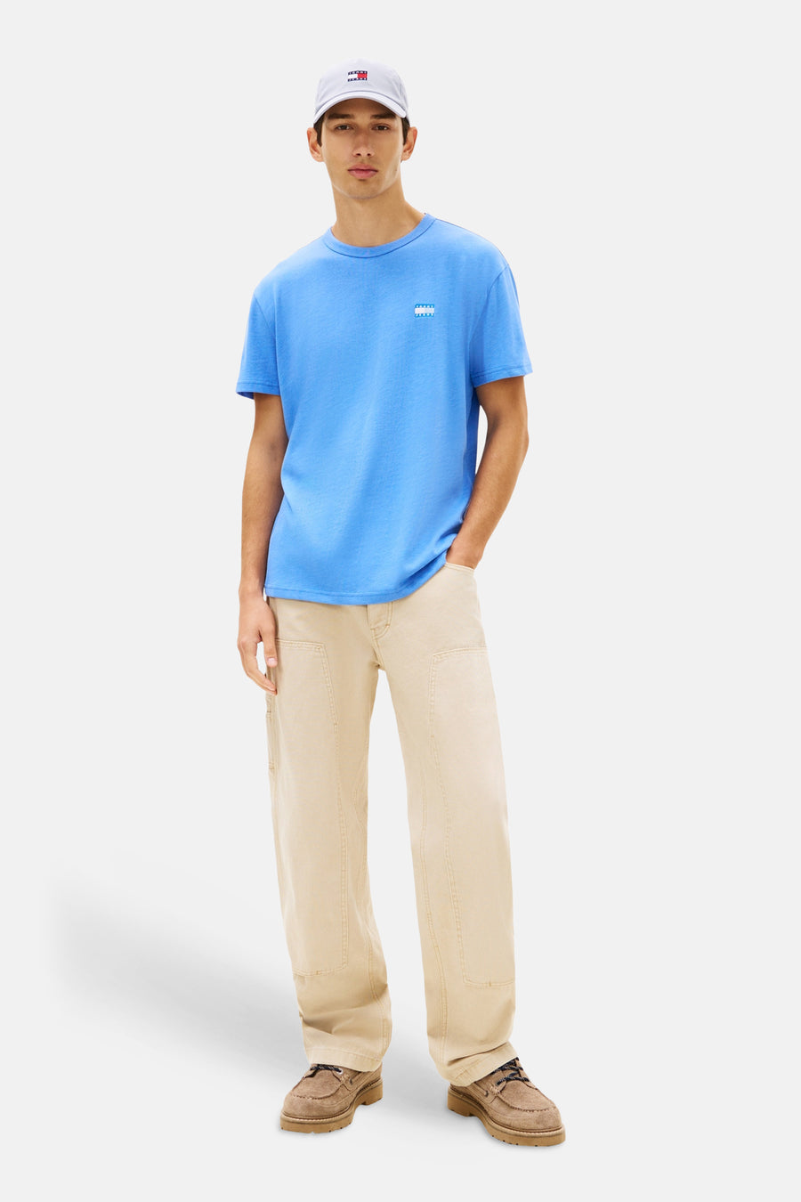 T-shirt bleu à manches courtes de TOMMY JEANS, porté avec un pantalon beige et des chaussures marron.