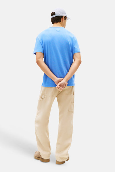 T-shirt bleu à manches courtes de Tommy Jeans, avec un logo subtil dans le cou, porté avec un pantalon beige ample.
