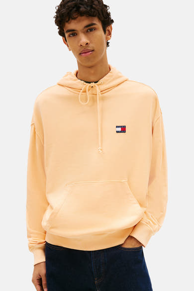 Oranje sweatshirt, van Tommy Jeans, met capuchon, kangoeroezak en logo op de borst, gedragen met een donkerblauwe jeans en zwarte schoenen.