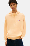 Oranje sweatshirt, van Tommy Jeans, met capuchon, kangoeroezak en logo op de borst, gedragen met een donkerblauwe jeans en zwarte schoenen.