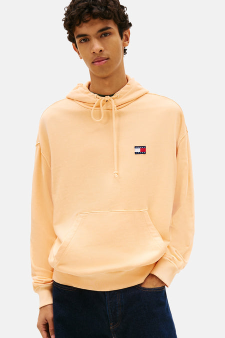 Oranje sweatshirt, van Tommy Jeans, met capuchon, kangoeroezak en logo op de borst, gedragen met een donkerblauwe jeans en zwarte schoenen.