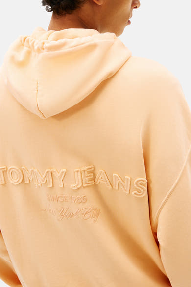 Oranje sweater van TOMMY JEANS met capuchon en geborduurd logo op de rug.