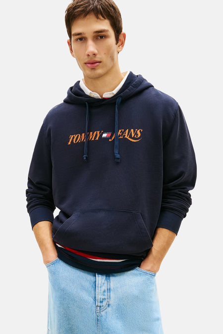 Blauwe Tommy Jeans hoodie, gedragen met een gestreept T-shirt en een verbleekte cargobroek, aangevuld met donkergroene schoenen.