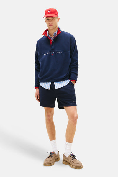 Short bleu de TOMMY JEANS, porté avec un pull molletonné et une chemise à carreaux.