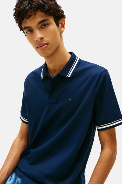 Polo à manches courtes bleu par TOMMY JEANS avec rayures blanches au col et aux manches courtes.
