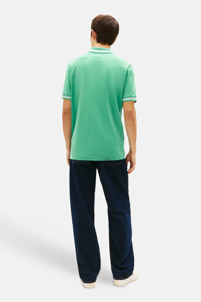 Groen poloshirt van TOMMY JEANS, met gestreepte kraag en mouwboorden, gedragen met een wijde jeans.
