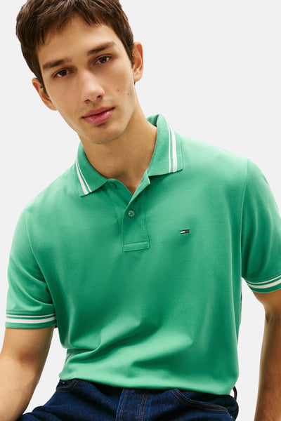 Groen gestreept poloshirt van TOMMY JEANS, met geborduurd logo en gedragen met een donkere spijkerbroek.