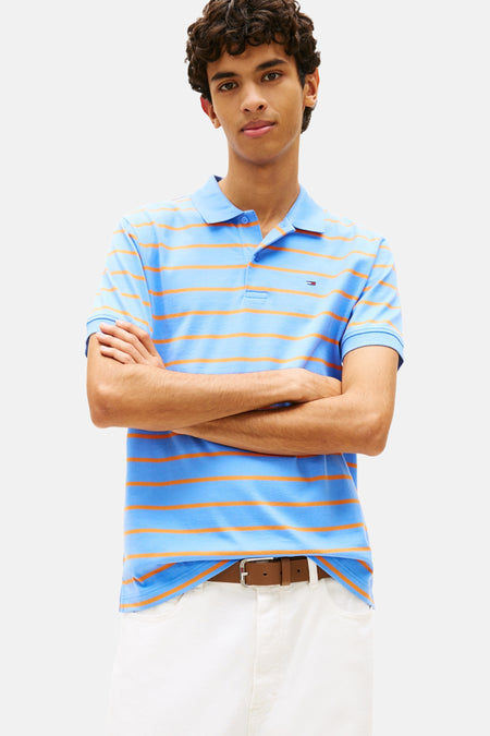 Blauwe gestreepte polo, van TOMMY JEANS, gedragen met een witte broek en bruine schoenen.