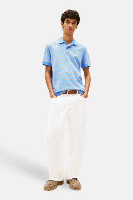 Polo bleu à rayures, de TOMMY JEANS, porté avec un pantalon blanc et des chaussures marron.