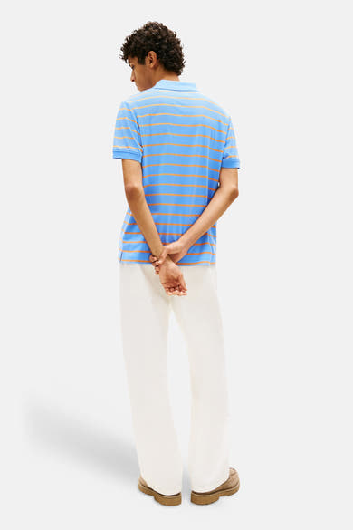 Blauwe gestreepte polo van TOMMY JEANS, gedragen met een wijde witte broek en bruine schoenen.