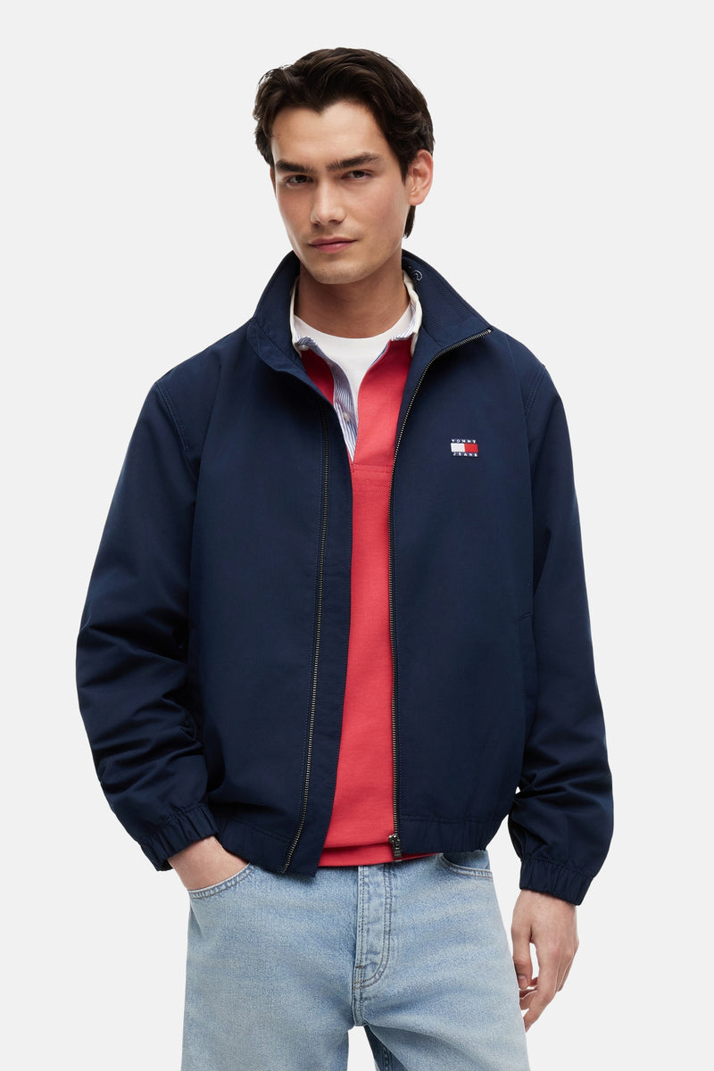 Blauwe regenjas van Tommy Jeans, met zilveren ritssluiting en logo op de borst.