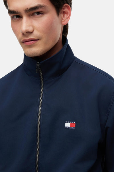 Veste de pluie bleue par Tommy Jeans, avec fermeture éclair argentée et logo sur la poitrine.