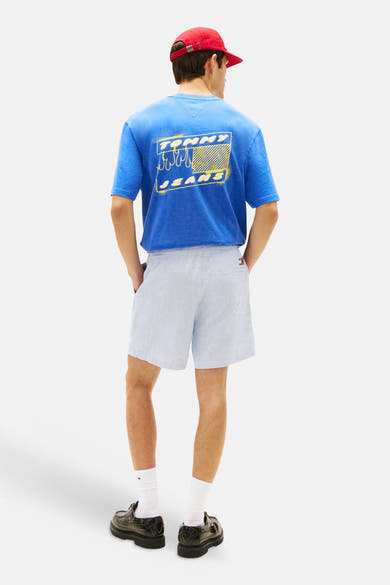 Lichtblauwe korte broek met strepen van TOMMY JEANS, gedragen met een blauw T-shirt met opdruk en een rode pet.