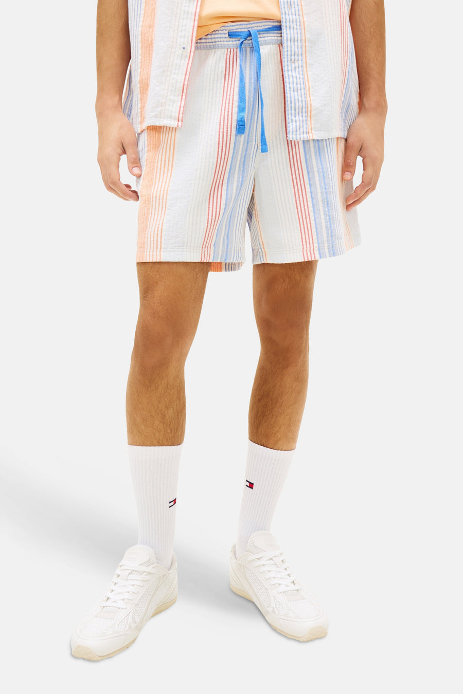 Short rayé orange par Tommy Jeans, avec cordon bleu, porté avec des chaussettes et des baskets blanches.