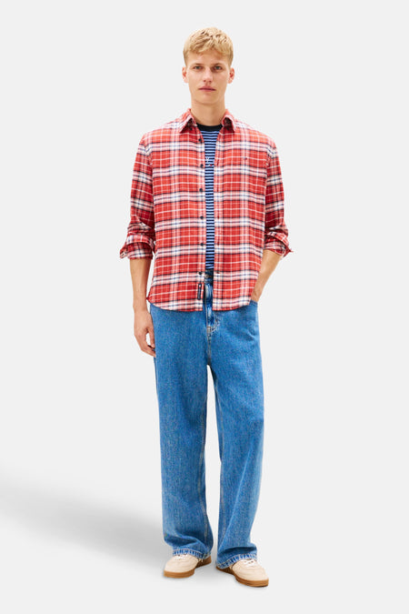 Chemise rouge à carreaux de TOMMY JEANS, portée sur un t-shirt rayé, avec un jean bleu ample.