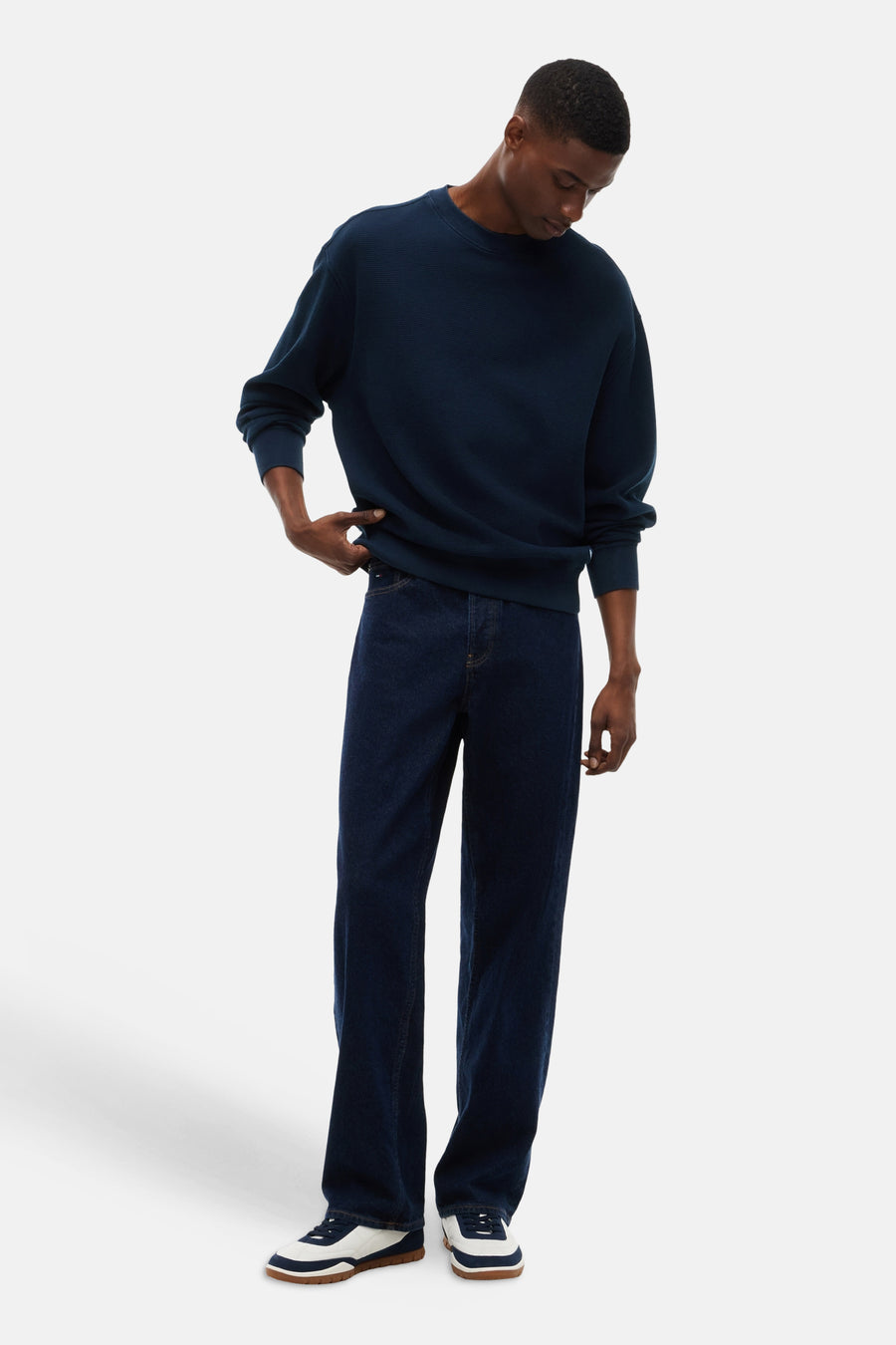 Navy blue ribbed crewneck sweatshirt with relaxed fit, worn with dark denim jeans and white sneakers, full-length lifestyle view