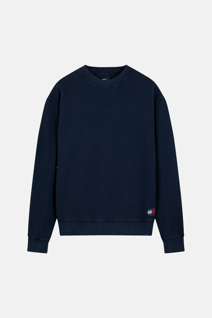Navy blue waffle-textured crewneck sweatshirt by Tommy Jeans, featuring ribbed cuffs and hem, with small flag logo on left sleeve, front view.