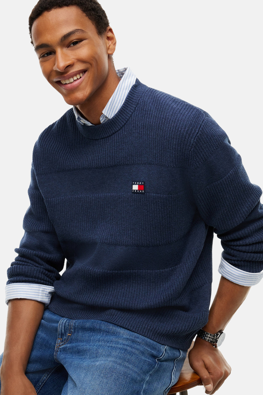 Navy ribbed crewneck sweater by Tommy Hilfiger with chest flag logo, worn over striped shirt, front view