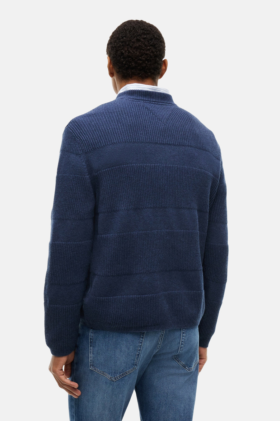 Blue ribbed knit crewneck sweater back view with horizontal textured panels, worn over white shirt with blue jeans