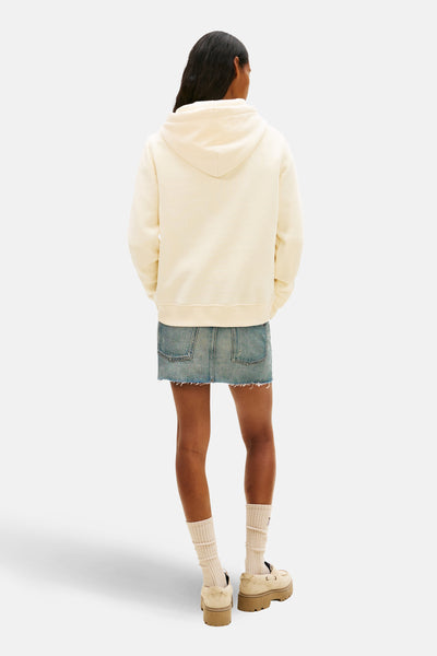 Sweat à capuche jaune crème de TOMMY JEANS, avec une jupe en jean bleu et des chaussures plateforme couleur crème.