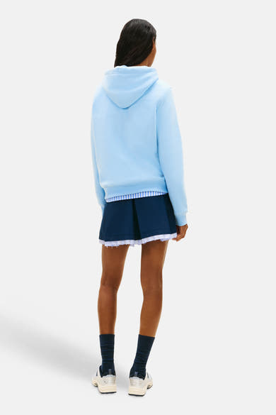 Blauwe hoodie van TOMMY JEANS, met een marineblauwe plooirok en marineblauwe sokken, van achteren gezien.