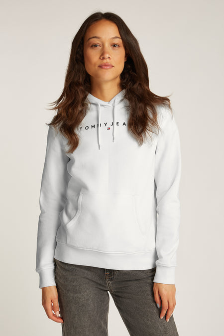 Witte hoodie van TOMMY JEANS, gedragen over een spijkerblouse, met een lichtblauwe jeans.