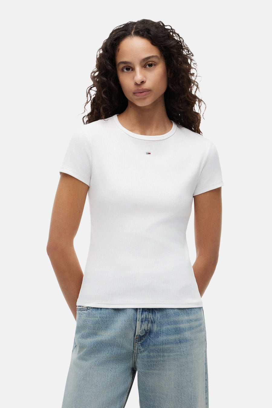 Top blanc uni côtelé à manches courtes de TOMMY JEANS, avec un petit logo sur la poitrine, porté avec un jean bleu.