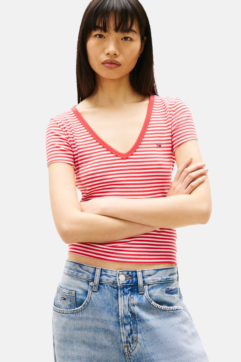 T-shirt rayé rouge et blanc de Tommy Jeans avec un col en V, porté avec un jean bleu.
