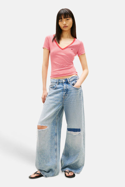 T-shirt multicolore à rayures de TOMMY JEANS, avec col en V et porté avec un jean ample déchiré.
