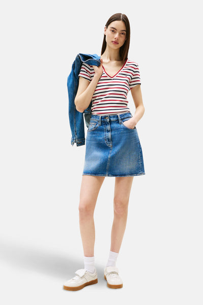 Multikleuren gestreept T-shirt van TOMMY JEANS, gedragen met een spijkerrok en een spijkerjasje over de schouder.