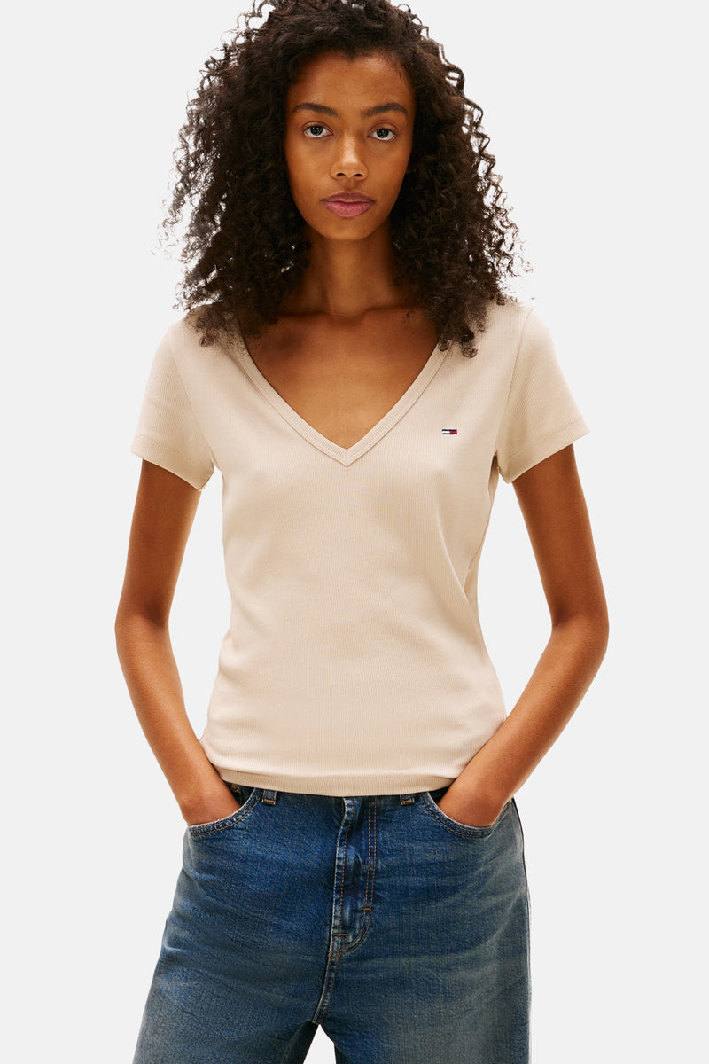 Beige T-shirt met korte mouwen van TOMMY JEANS, gedragen met een gestreepte trui en een wijde jeans met omgeslagen zoom.