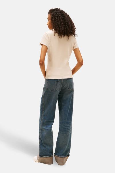 Beige T-shirt met korte mouwen van TOMMY JEANS, gedragen met een wijde blauwe jeans en witte sportschoenen.