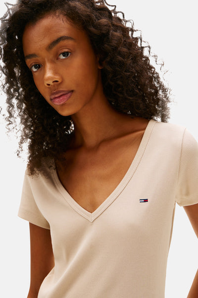T-shirt beige à col V en maille côtelée de Tommy Jeans, porté par une femme aux cheveux bouclés.