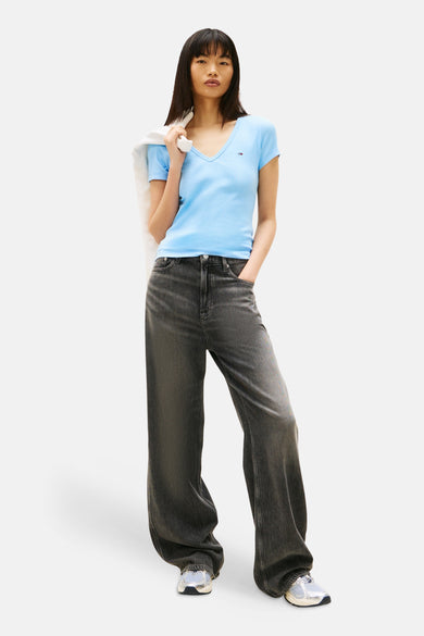 T-shirt bleu à manches courtes de TOMMY JEANS, porté avec un pantalon large gris et des chaussures de sport argentées.