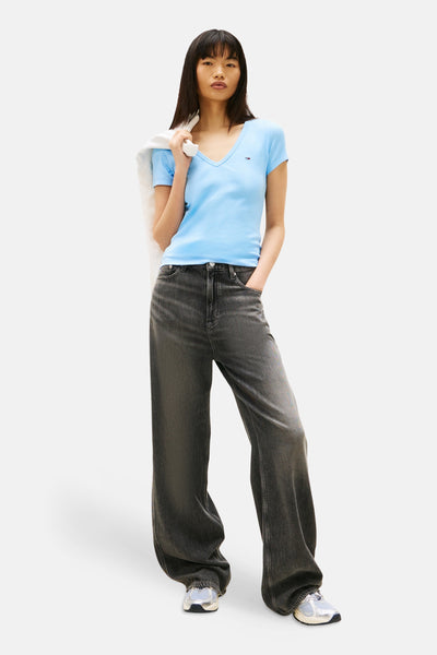 T-shirt bleu à manches courtes de TOMMY JEANS, porté avec un pantalon large gris et des chaussures de sport argentées.