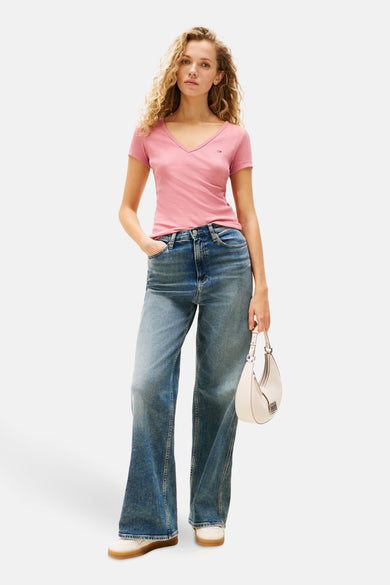 Roze T-shirt met korte mouwen van TOMMY JEANS, gedragen met een wijde jeans en een witte handtas.