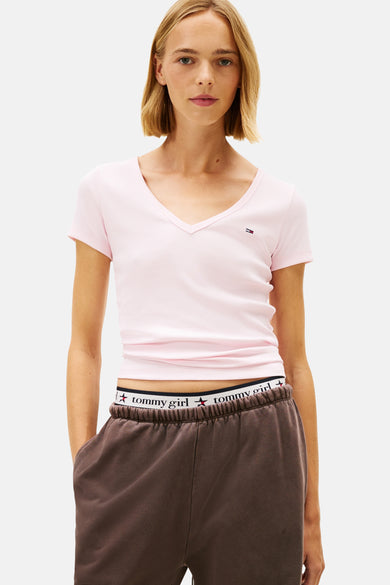 T-shirt rose à manches courtes de TOMMY JEANS avec un col en V, porté avec un pantalon de survêtement marron.