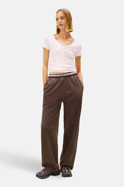 T-shirt rose à manches courtes de TOMMY JEANS, porté avec un pantalon de survêtement marron et des chaussures de sport.