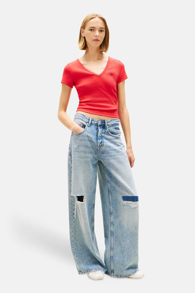 T-shirt rouge à manches courtes de Tommy Jeans, porté avec un jean ample destroy et des baskets blanches.
