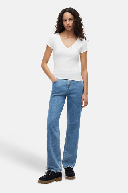 Top blanc uni côtelé de TOMMY JEANS, col en V, petit logo, porté avec jean et chaussures foncées.