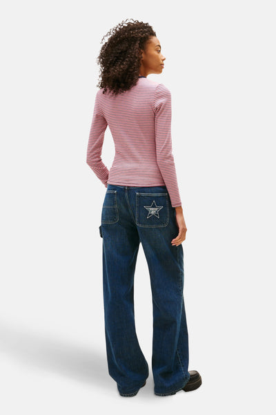 Multikleuren T-shirt met lange mouwen van TOMMY JEANS, gestreept met een persoon die een zwarte jeans en schoenen draagt.