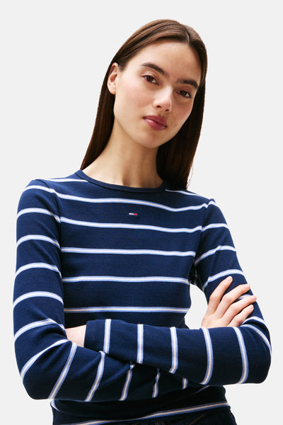 Blauwe T-shirt met lange mouwen van TOMMY JEANS, witte horizontale strepen, gedragen door een vrouw.