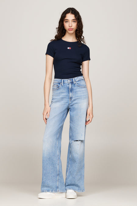 T-shirt bleu à manches courtes de TOMMY JEANS, porté avec un jean ample déchiré et des baskets blanches.
